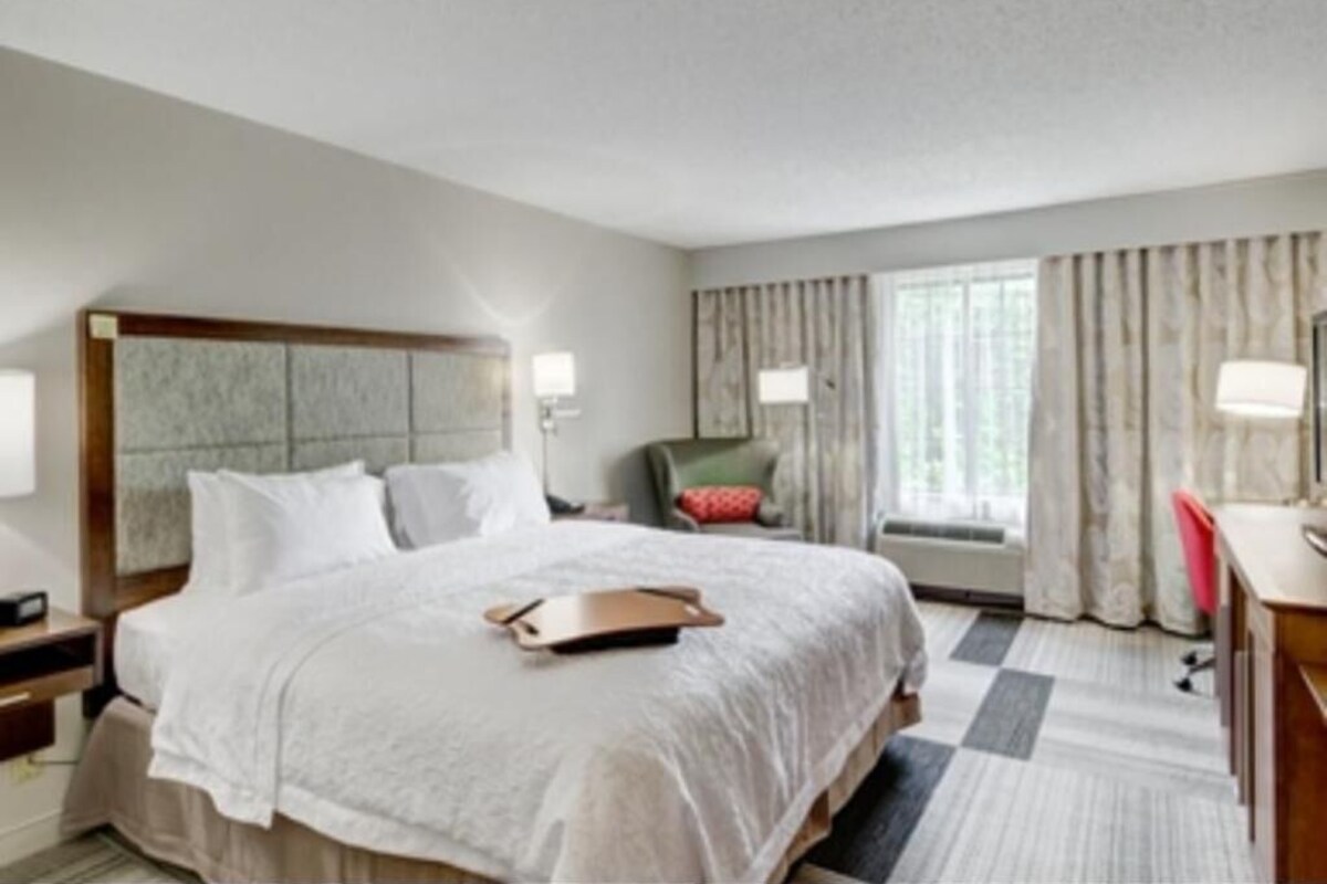 A hotel room with a large bed, a desk, a chair, and a window with curtains.