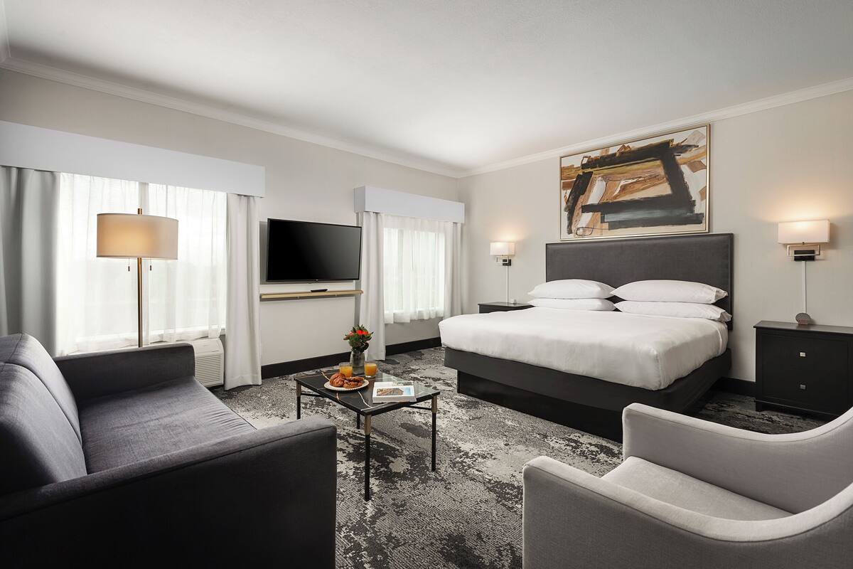 A modern hotel room with a large bed, a flat-screen TV, a sofa, a coffee table, and a painting on the wall.