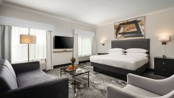 Une chambre d’hôtel moderne avec un grand lit, un téléviseur à écran plat, un canapé, une table basse et un tableau au mur.