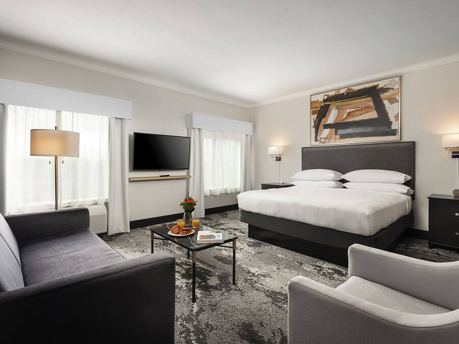 Une chambre d’hôtel moderne avec un grand lit, un téléviseur à écran plat, un canapé, une table basse et un tableau au mur.