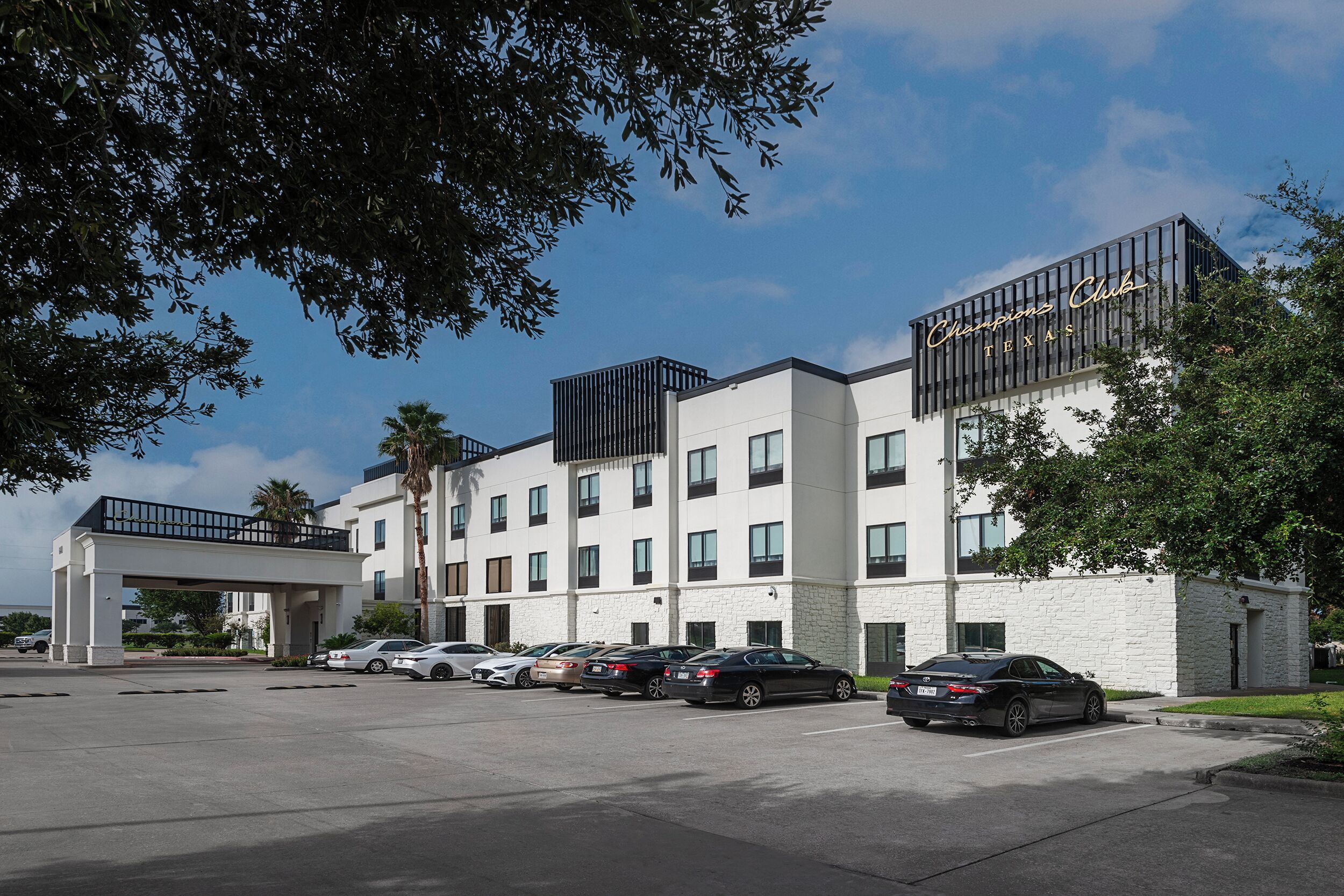 Et hotel med moderne design, med en hvid facade og et skilt der siger "Champions Club Texas".