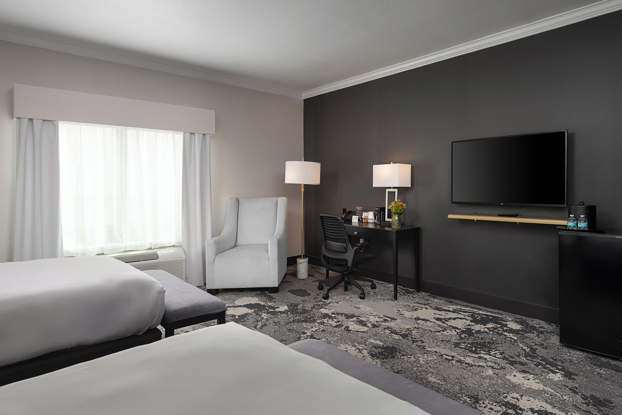 A hotel room with two beds, a desk with a chair, a TV, and a lamp.