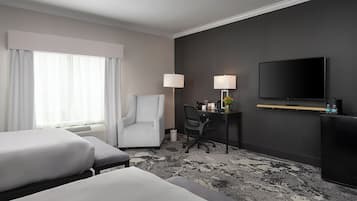 A hotel room with two beds, a desk with a chair, a TV, and a lamp.