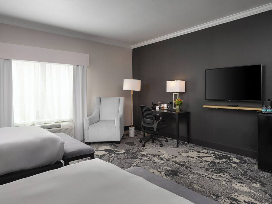 Quarto de hotel com duas camas, uma secretária com cadeira, televisão e uma luminária.
