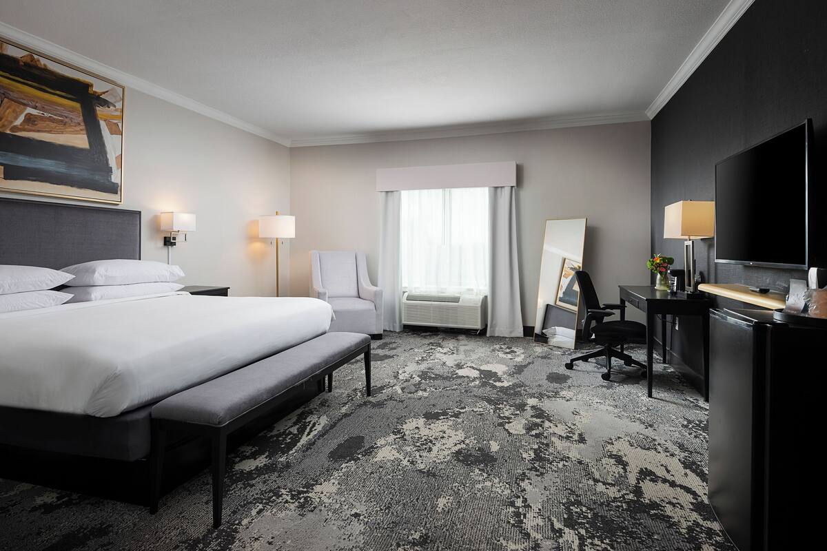 A hotel room with a large bed, a desk, a chair, a TV, and a painting on the wall.