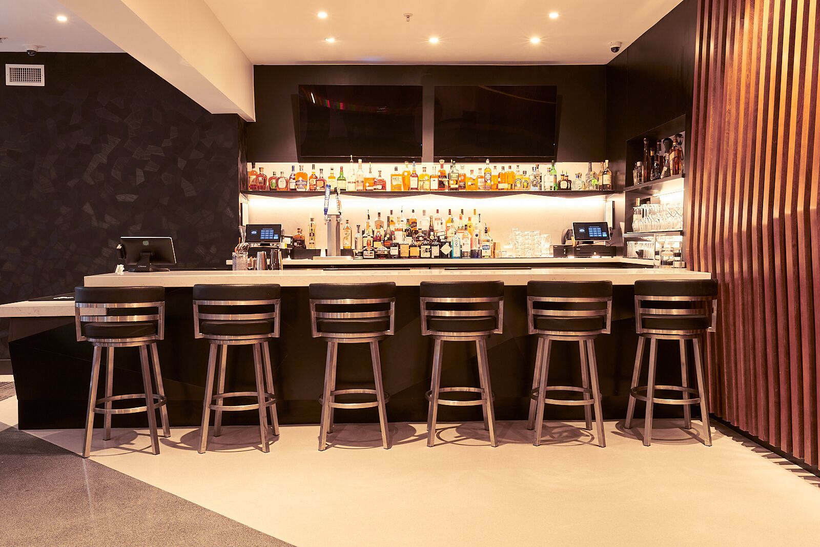 Una zona de bar con una barra larga, varios taburetes y una amplia variedad de botellas.
