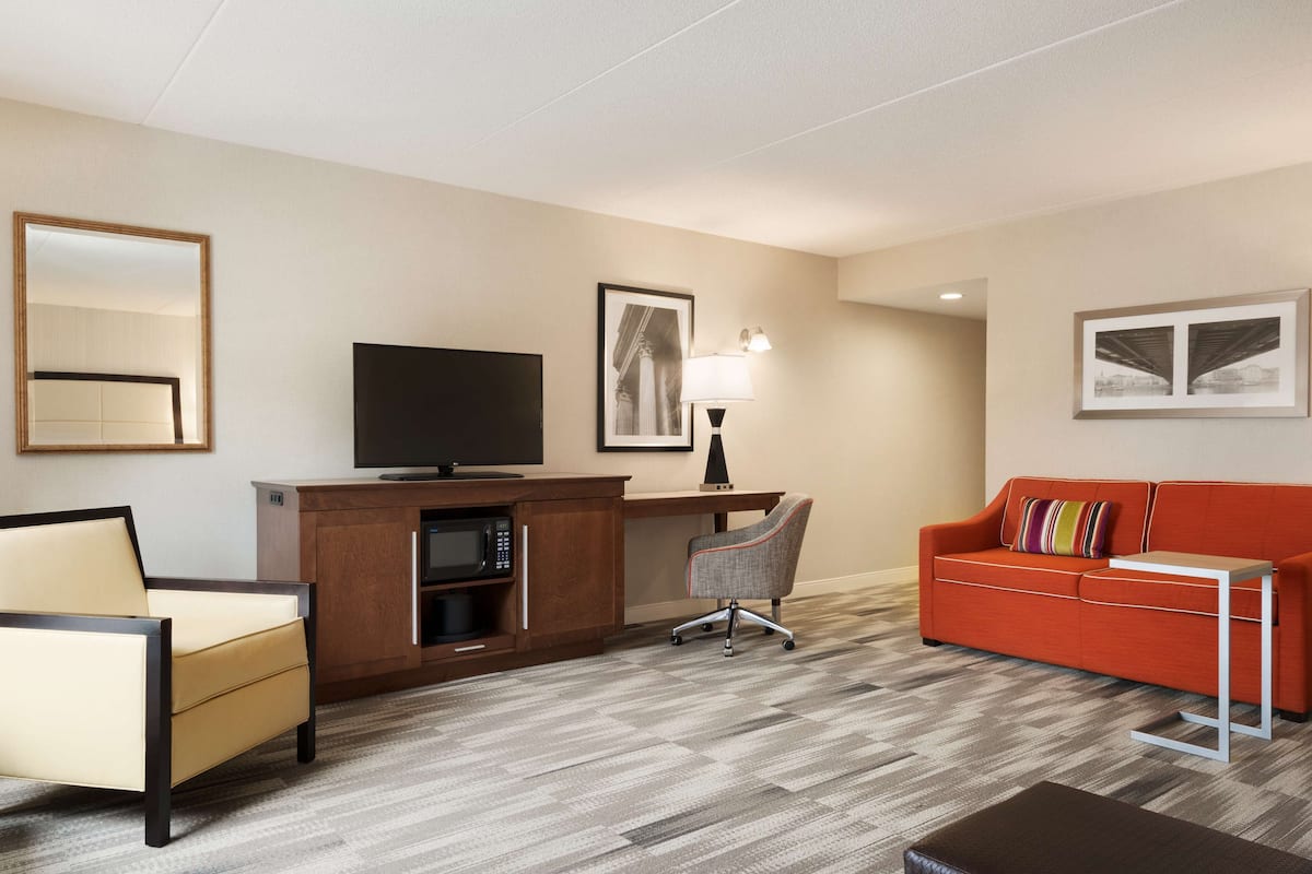 Una habitació d'hotel amb un llit, una escriptori amb un ordinador, una televisió, un sofà i una làmpada.