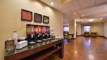 A hotel breakfast area with a coffee station, seating, and a view of the dining area.