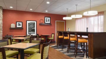 A restaurant with multiple tables and chairs, a bar area, and framed pictures on the walls.