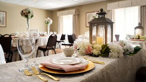 Mesa de jantar posta com pratos, copos e talheres, decorada com flores e um candeeiro.