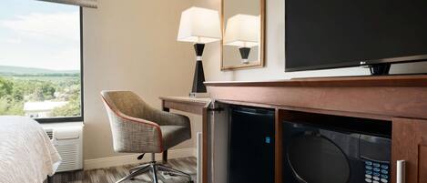 Una habitación de hotel con una cama, un escritorio con lámpara, televisión y microondas.
