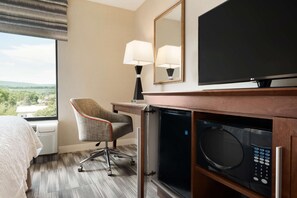 A hotel room with a bed, a desk with a lamp, a television, and a microwave.