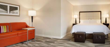 A hotel room with a bed, a sofa, two bedside tables, and a carpeted floor.