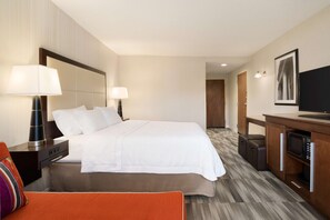 A hotel room with a large bed, bedside lamps, a television, a desk with a microwave, and a suitcase.