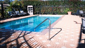 A swimming pool with a metal ladder, surrounded by a brick patio and lounge chairs.
