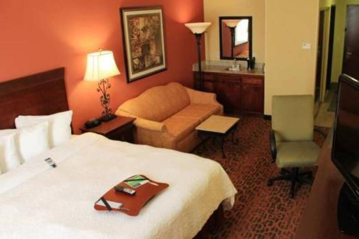 A hotel room with a bed, a sofa, a desk, a lamp, and a mirror.
