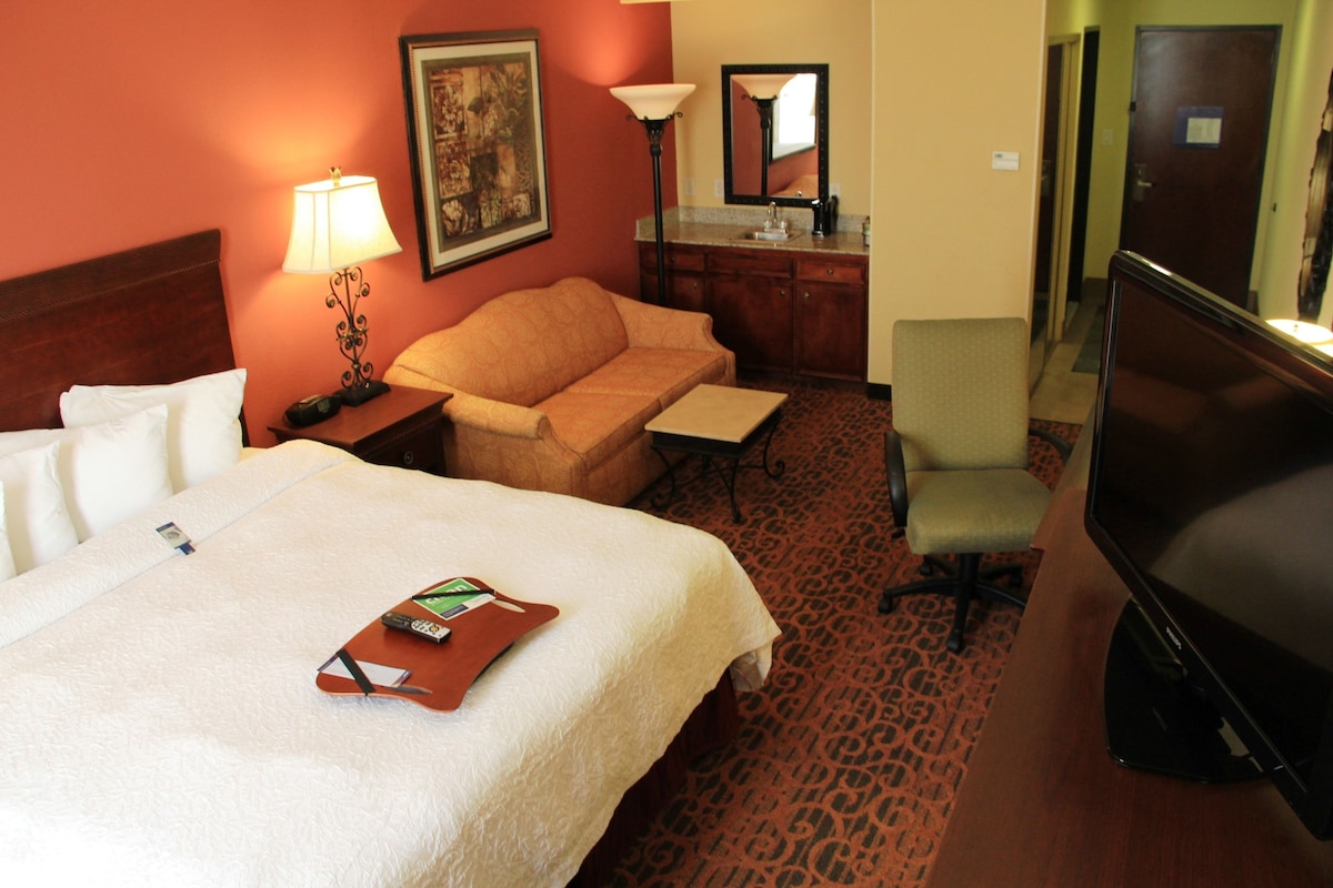A hotel room with a large bed, a sofa, a desk, a television, and a bathroom.