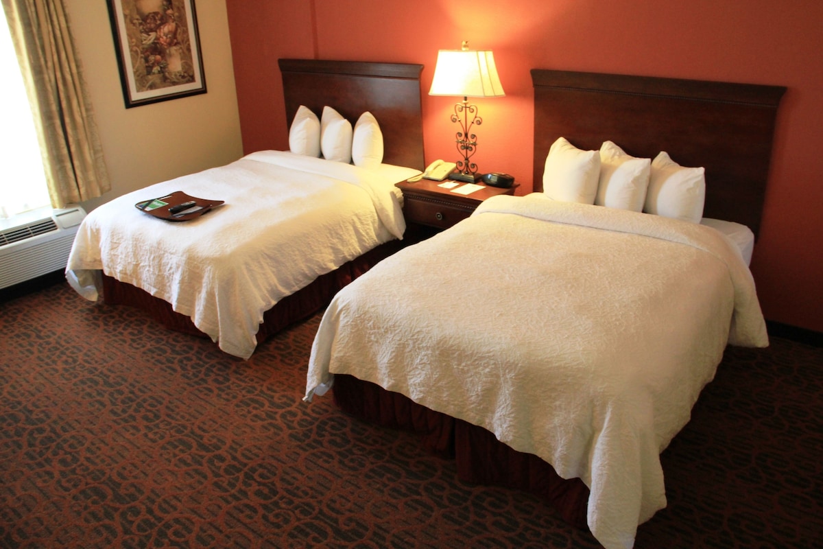 Two single beds with white linens, a bedside table with a lamp, and a patterned carpet.
