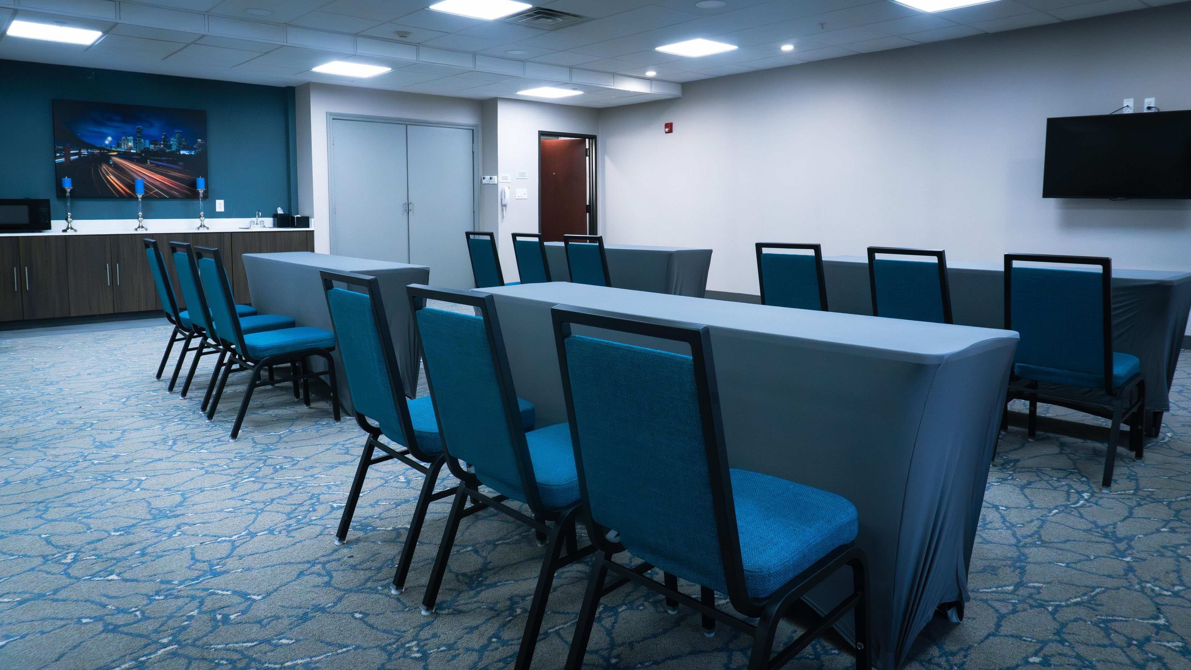A conference room with rows of chairs, a table, a painting, and a television on the wall.