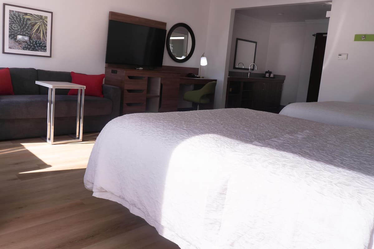 A hotel room with a large bed, a desk, a chair, a TV, and a bathroom with a mirror and sink.