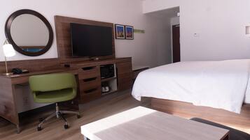 A hotel room with a bed, a desk with a chair, a television, a mirror, and a small shelf with a microwave.