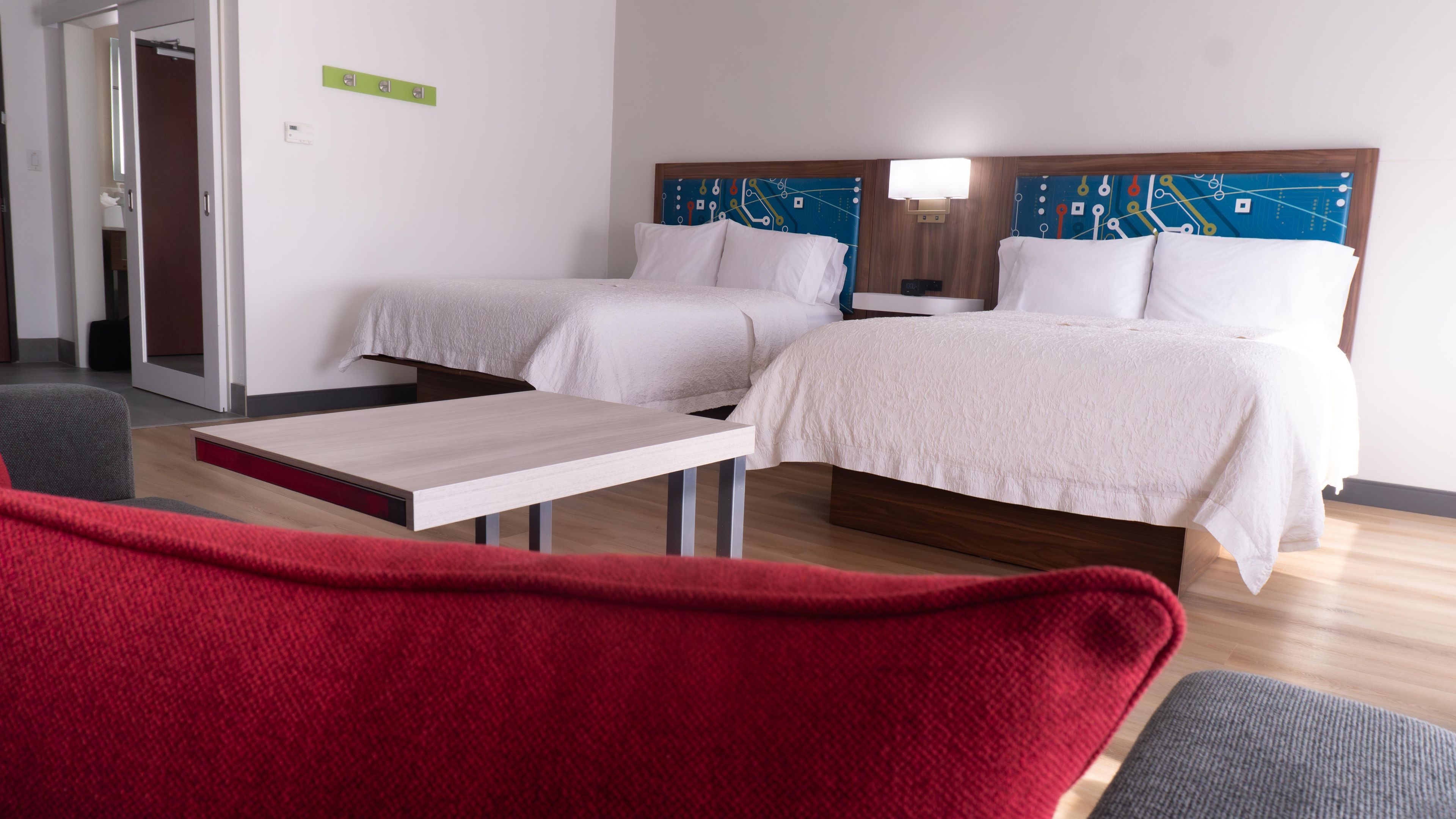 Una habitación de hotel con dos camas, una mesita y una silla roja.