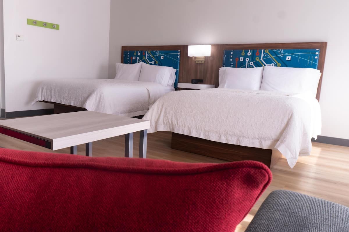 A hotel room with two beds, a small table, and a red chair.