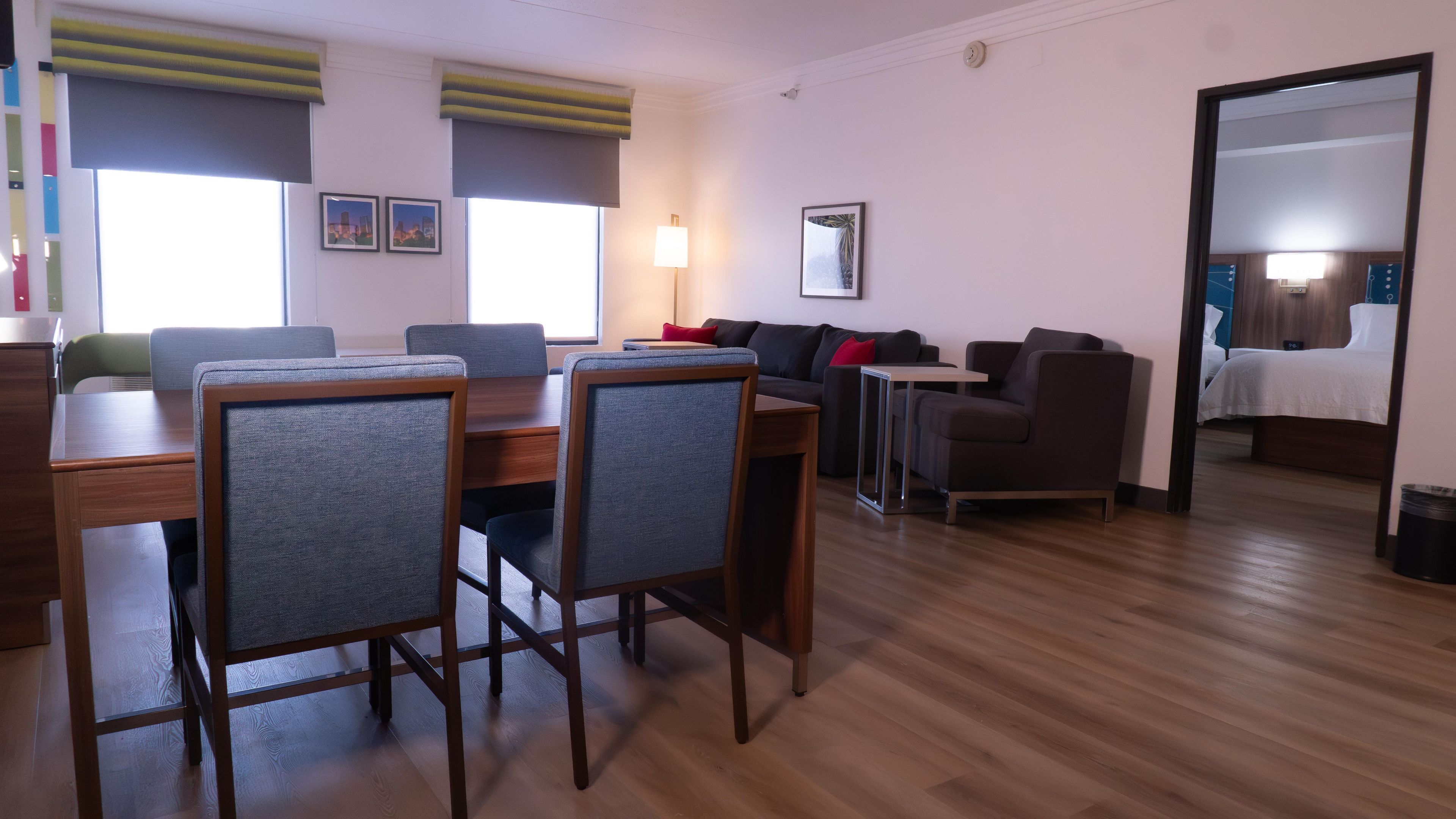 A modern living room with a dining area, wooden flooring, and a large mirror reflecting the room.