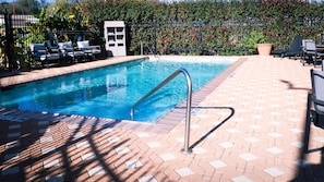 A swimming pool with a metal ladder, surrounded by lounge chairs and a brick patio. - Hampton Inn & Suites Houston Katy (Katy)