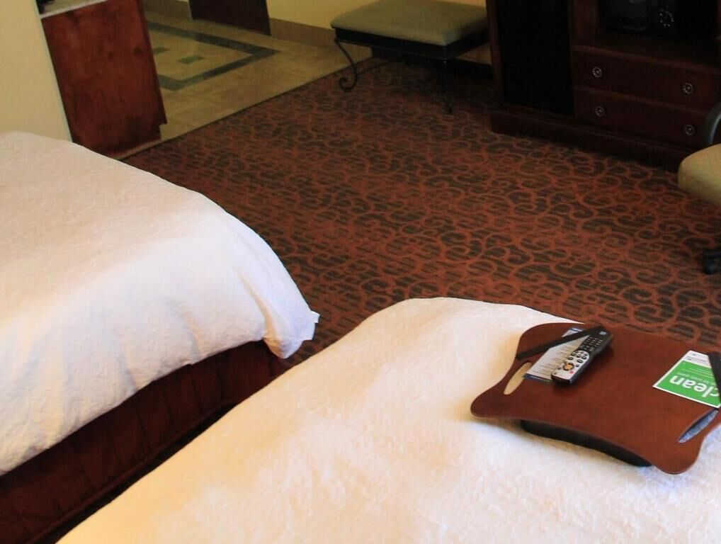 Habitación de hotel con dos camas, un pequeño banco, un aparador de madera y un mando a distancia sobre una bandeja.