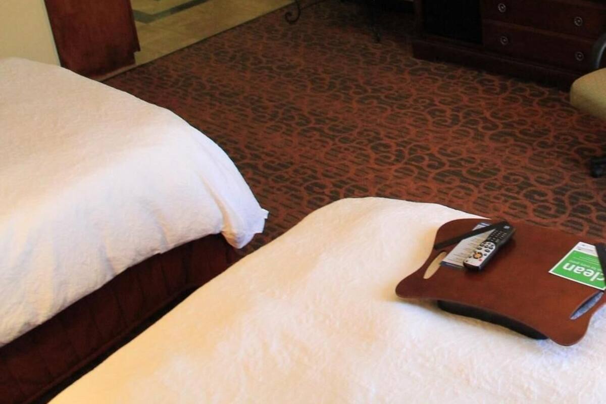 Habitació d'hotel amb dos llits, una petita banca, un taulell de tocador de fusta i un comandament a distància sobre un safata.