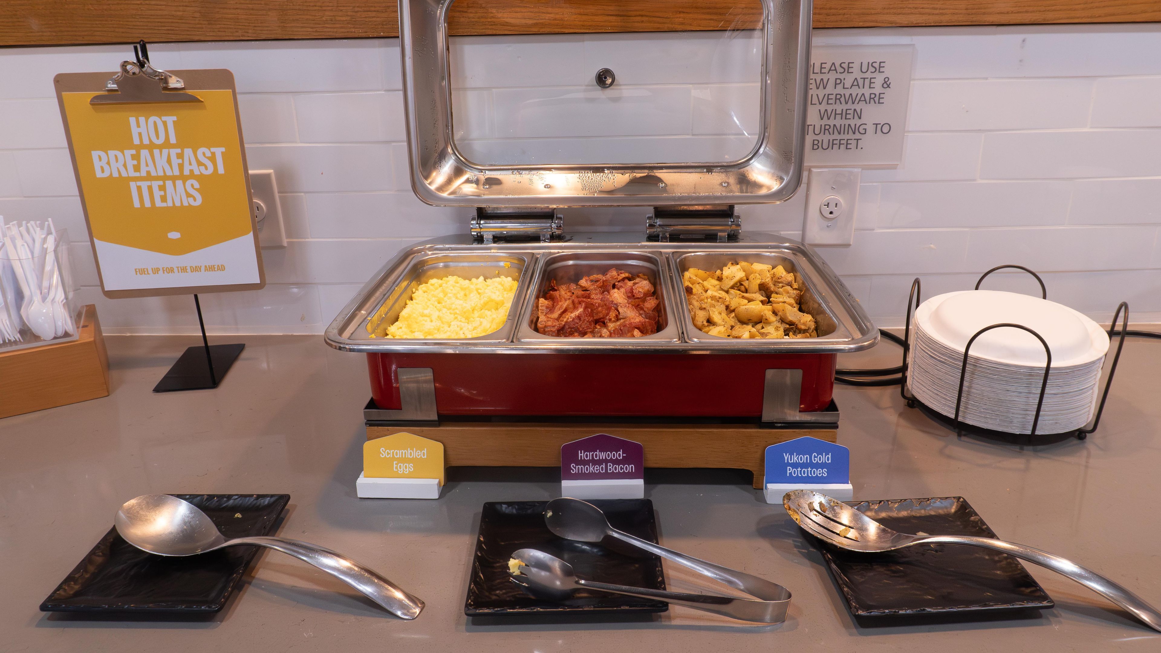 A buffet setup with labeled food items including scrambled eggs, smoked bacon, and Yukon gold potatoes.