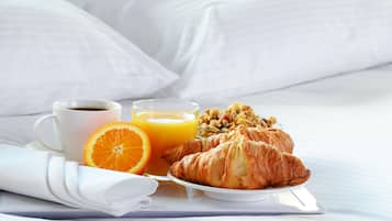 Desayuno con cruasanes, zumo de naranja y café sobre una cama con ropa blanca.