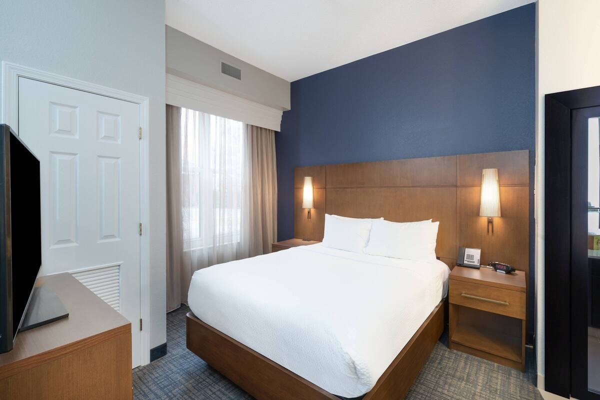 A hotel room with a large bed, bedside tables, a TV, and a window with curtains.