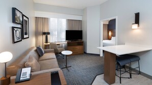 Une chambre d’hôtel équipée d’un canapé, d’un bureau, d’une télévision, d’une petite table et d’un coin bar.