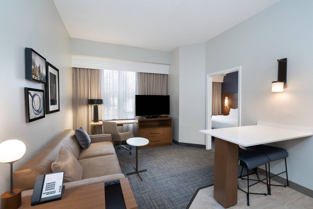 A hotel room with a sofa, a desk, a TV, a small table, and a bar area.