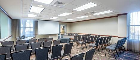 A conference room with rows of chairs, a projector screen, and a large table.