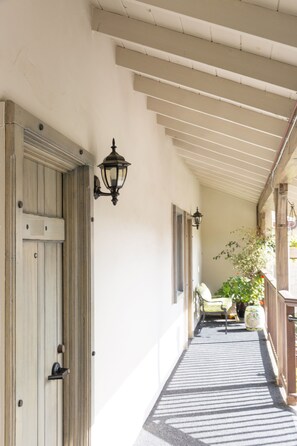 A corridor with a wooden door, a wall-mounted lantern, a bench, and a potted plant.