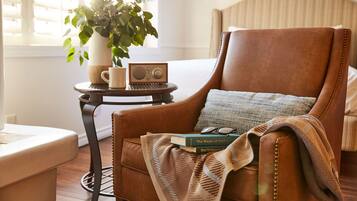 A cozy room with a leather armchair, a small round table with a radio, a potted plant, and a bookshelf with books.