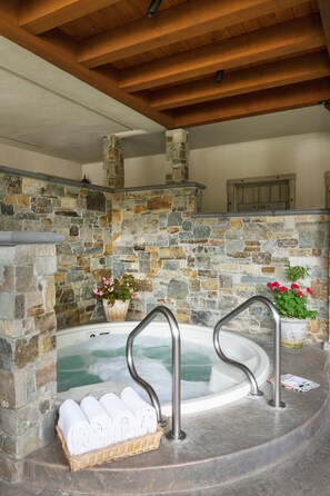 A stone-walled hot tub with metal railings, surrounded by a stone wall and wooden beams. - Coachman's Inn, A Four Sisters Inn (Carmel)