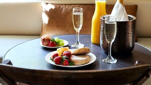 Une table ronde dressée pour le petit-déjeuner, avec une bouteille de champagne, un verre de jus d’orange et une assiette de fruits frais et de viennoiseries.
