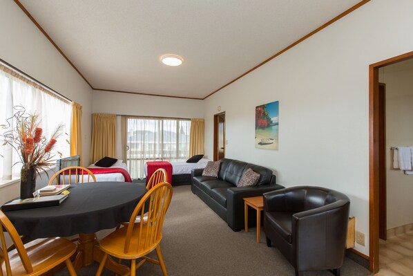 A furnished living room with a dining table, chairs, a sofa, and a small side table. - Summit Motor Lodge (Tauranga)