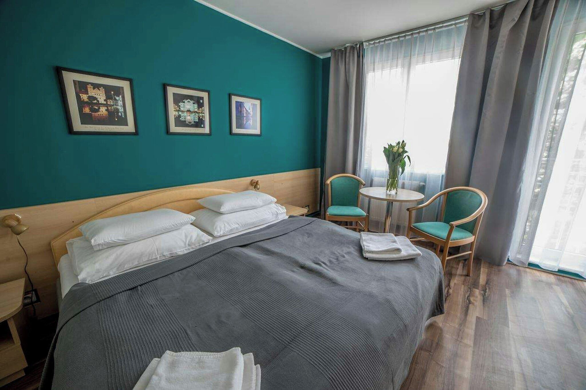 A hotel room with a bed, two chairs, a small table, and curtains.