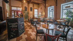 A cafe interior with wooden beams, brick walls, and a chalkboard menu. Tables and chairs are arranged for seating. - Teledom Hotel & Conference Center (Kosice)