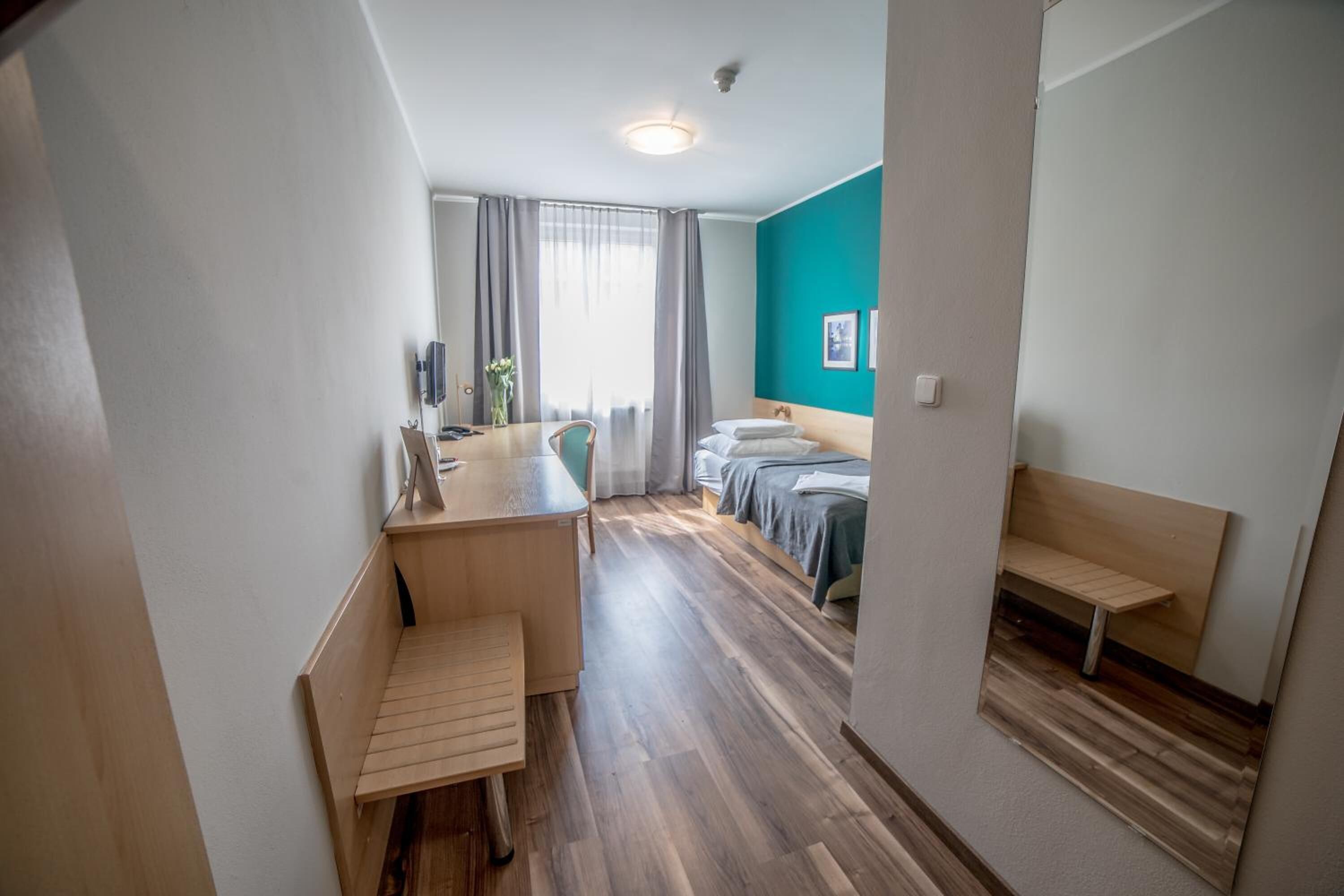 Habitación de hotel compacta con escritorio de madera, una cama, un banco y una pequeña mesa.