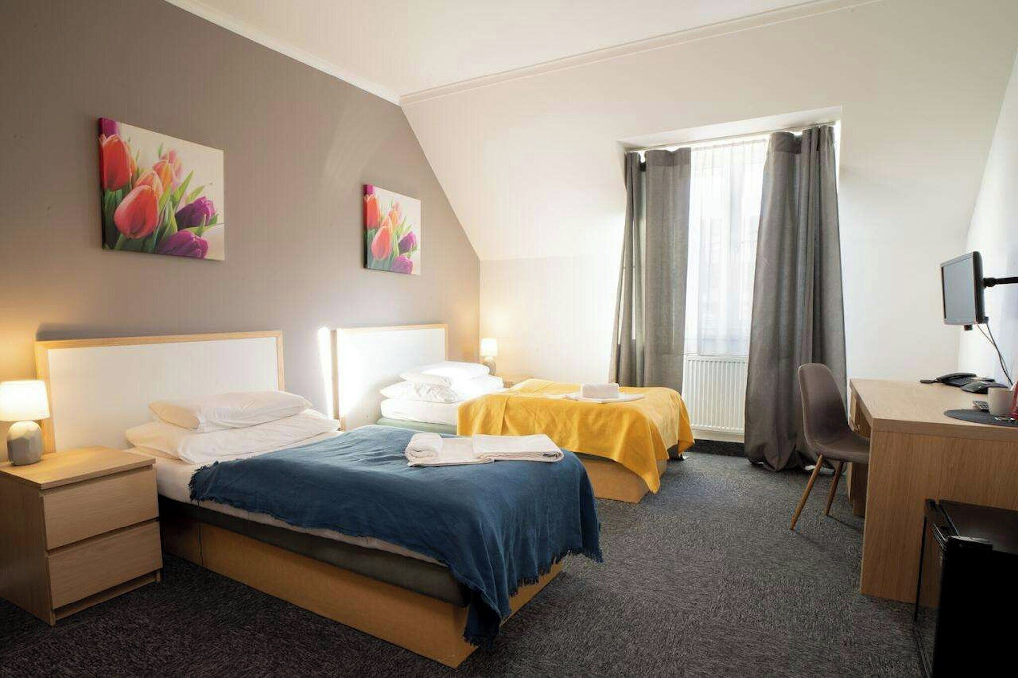 A hotel room with two beds, a desk, a chair, and a television.