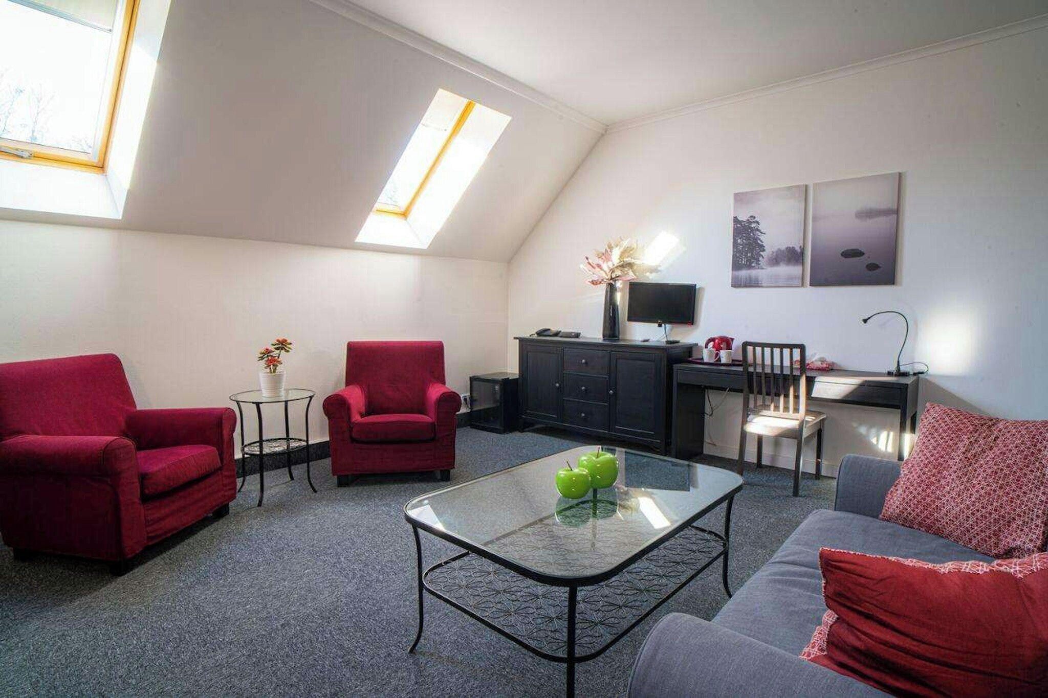 Una sala moderna con sofás rojos, una mesa de centro de vidrio y un escritorio con una computadora.