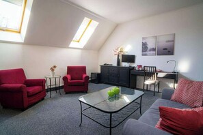 A modern living room with red sofas, a glass coffee table, and a desk with a computer. - Teledom Hotel & Conference Center (Kosice)