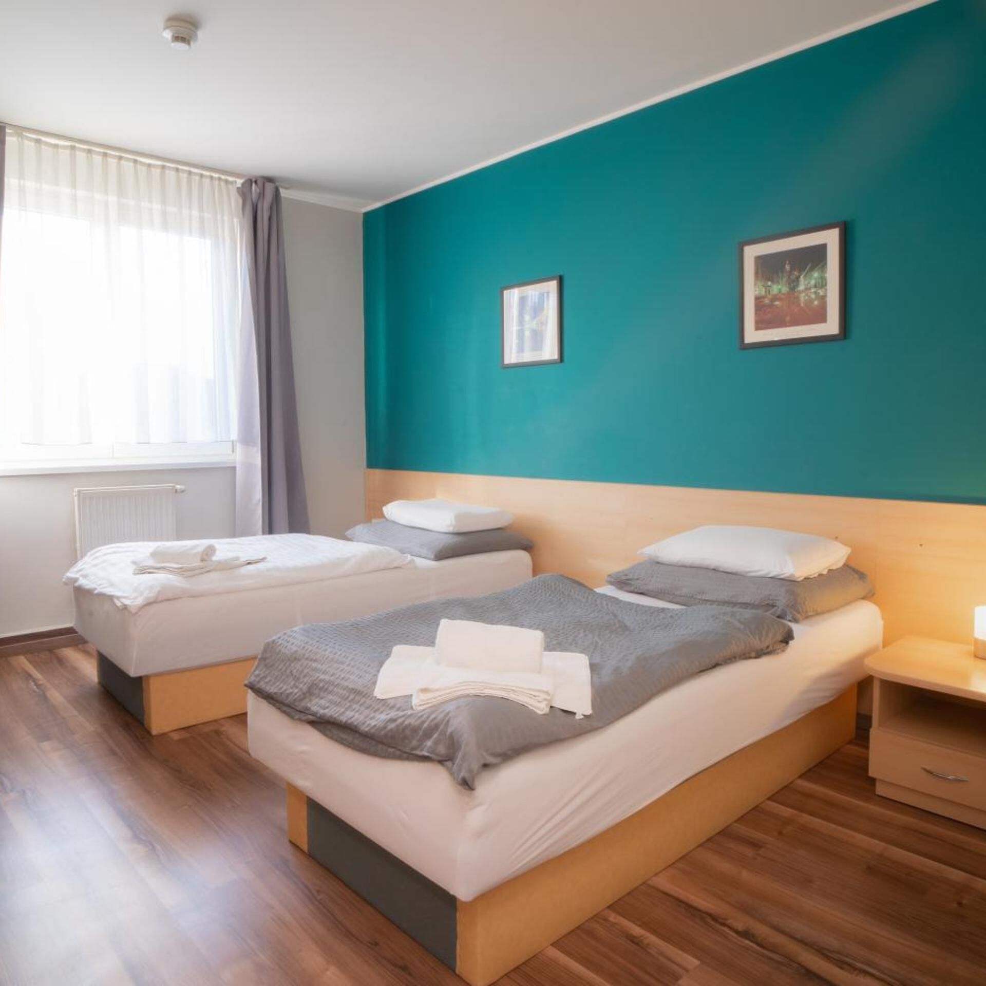Une chambre d’hôtel avec deux lits, une fenêtre avec des rideaux, un mur d’accent de couleur turquoise et un tableau encadré.