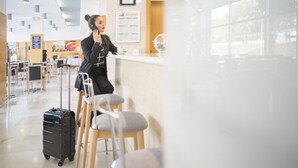 A person sitting at a bar with a suitcase and a laptop, in a well-lit indoor space with tables and chairs. - Holiday Inn Express Valencia - Bonaire by IHG (Quart de Poblet)